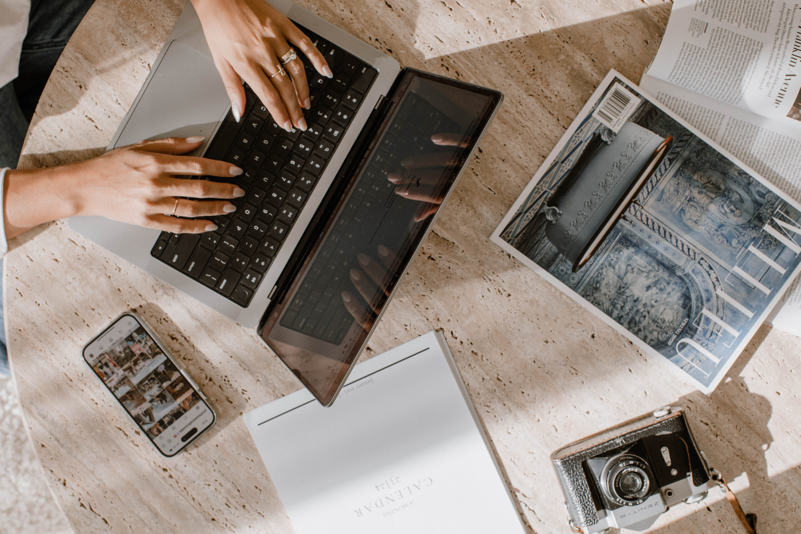 Content creator juggling tasks with laptop, notebook, and creative tools at a workspace