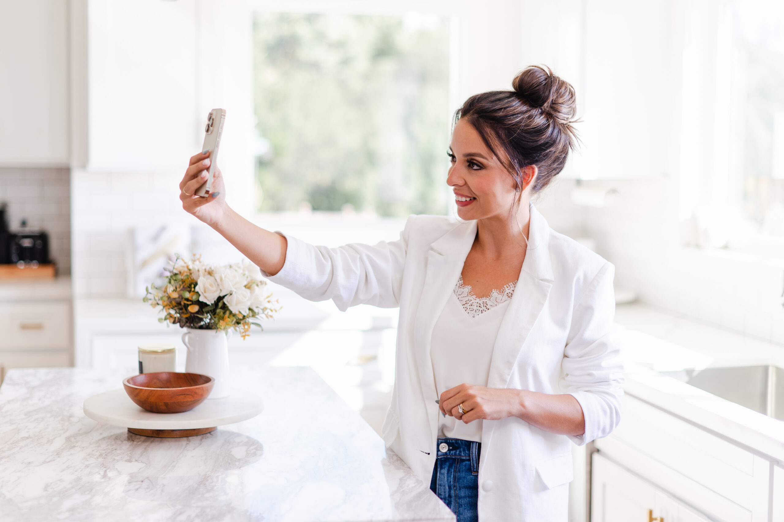 Smiling influencer recording an Instagram Story on her smartphone in a bright, modern kitchen, showcasing behind-the-scenes content creation to improve Instagram story quality.