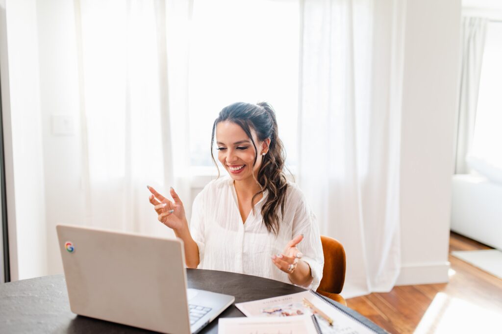 Smiling influencer in a bright, modern home setting, engaging with her laptop during a virtual meeting or creating content. Ideal for a blog post about pitching paid brand deals and influencer strategies.